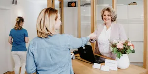 Empfang der Praxis: Mitarbeiterin begrüßt eine Patientin am Tresen